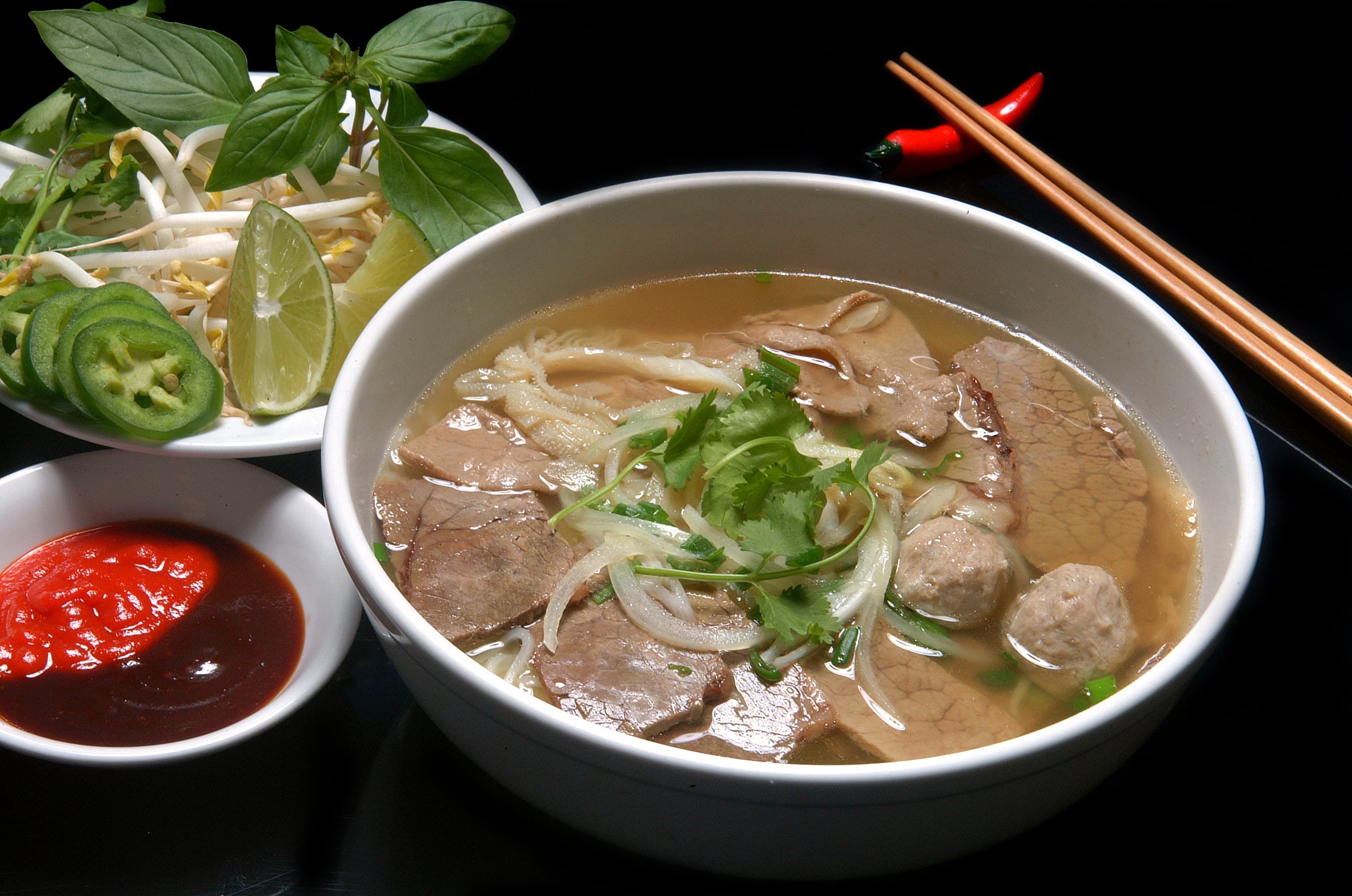 A steaming bowl of pho with fresh herbs, bean sprouts, and chopsticks